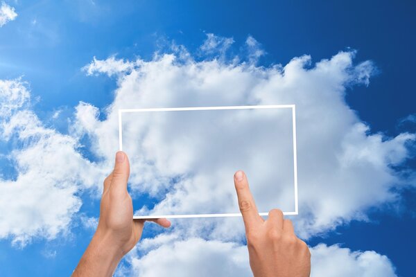 Mains tenant un écran de tablette transparent sur un fond de nuages.