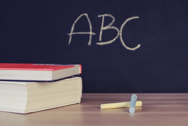 Photo d'un tableau où est marqué "ABC" et d'un bureau où sont posées deux craies et deux livres